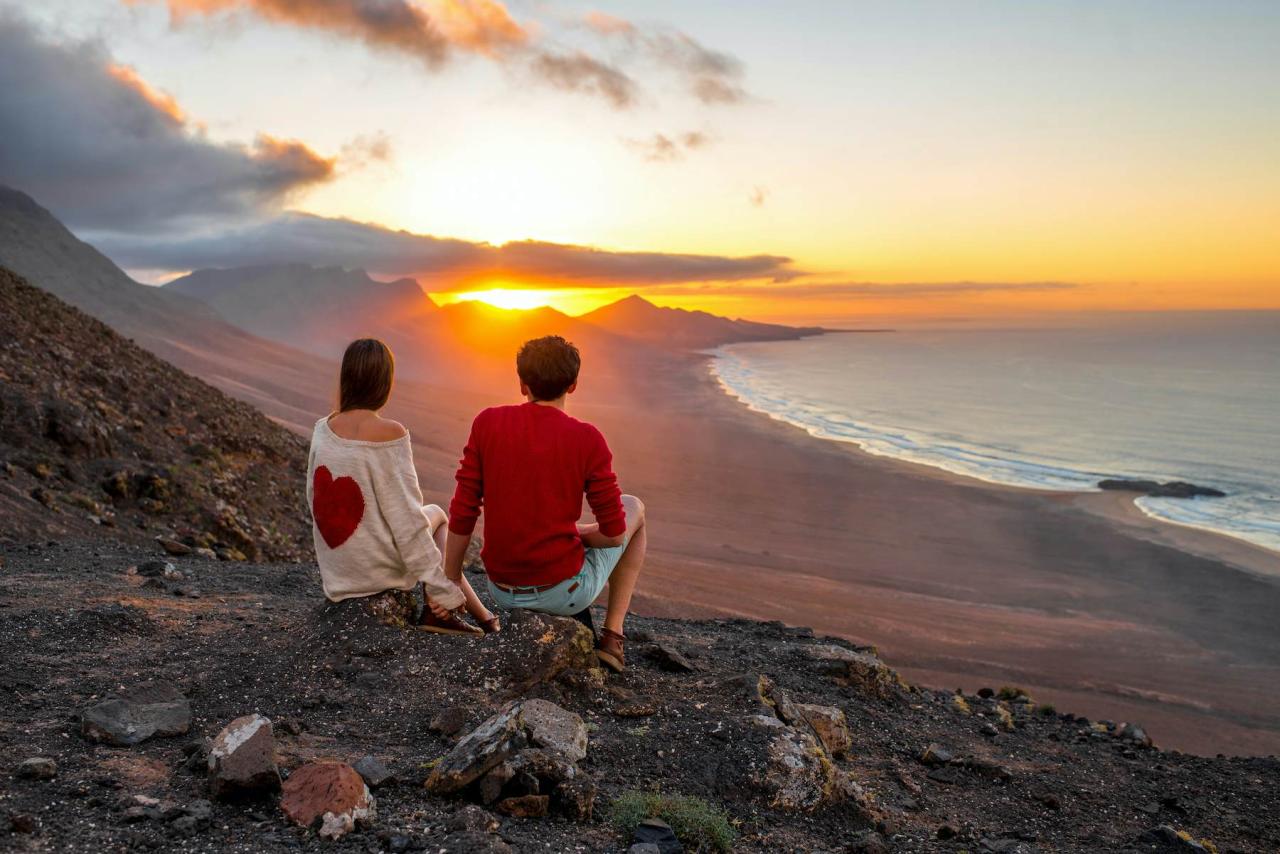 Ungt par nyter vakker solnedgang som sitter sammen på fjellet med flott utsikt over Cofete-kysten på Fuerteventura-øya.